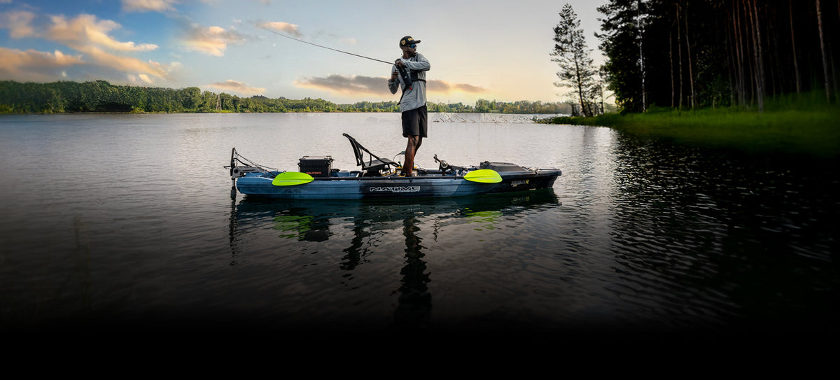 An angler standing and casting from a Native Watercraft Hammer 1210 Propel Pedal Kayak on a calm lake at sunrise