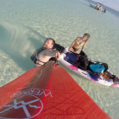 Man and woman on a sandbar in the ocean with kayaks.